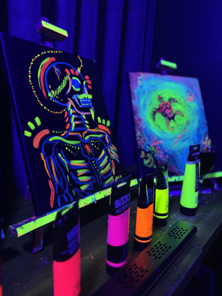 Toiles peintes avec de la peinture fluorescente sous lumière UV, représentant un squelette coloré et une tortue, exposées lors d’un atelier peinture dans le noir à Paris.