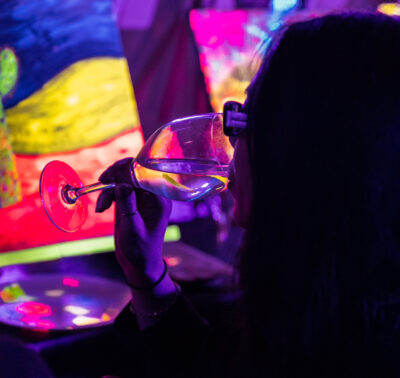 Femme buvant un verre de vin devant sa toile fluorescente lors d’un atelier de peinture dans le noir à Paris